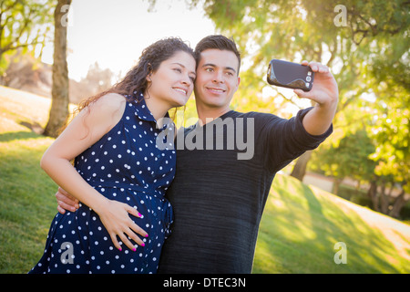 Moglie incinta e il marito tenendo Telefono Cellulare una foto di loro stessi all'aperto presso il parco. Foto Stock