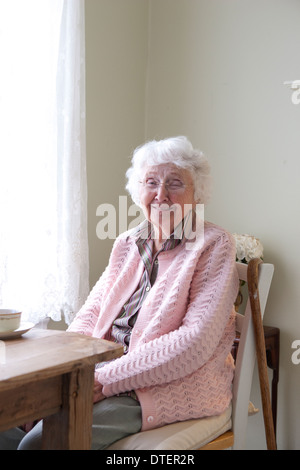 Sorridente donna anziana seduta a tavola con la tazza di tè Foto Stock