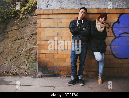 Bella giovane uomo e donna in abiti caldi insieme in piedi poggiando su un muro esterno. Asian adolescente matura in posa Foto Stock