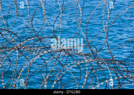 Primo piano della avvolto filo di rasoio scherma i modelli e le texture contro il mare blu-Fondo di acqua Foto Stock