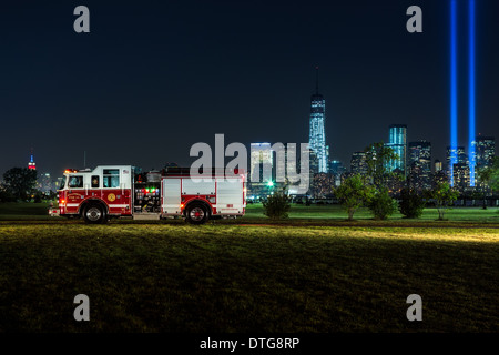 Hillcrest Fire azienda numero 1 firetruck con una vista sullo sfondo dello skyline di New York City con l' Empire State Building illuminati in rosso, bianco e blu, la nuova libertà torre situata in corrispondenza di una World Trade Center e i due fasci di luce dal tributo alla luce memoriale sulla Septermber 11th, 2013. Foto Stock