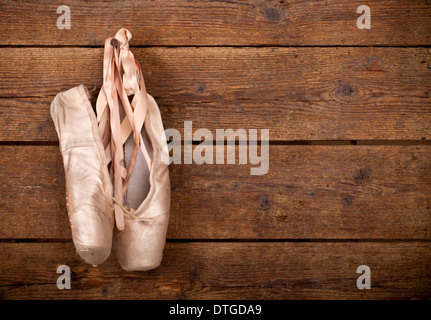 Vecchio usato rosa scarpe da ballo appesi su sfondo di legno Foto Stock