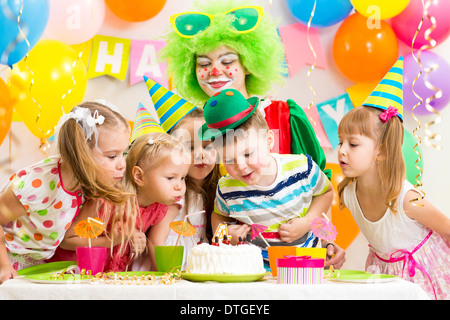 I bambini con clown celebrare la festa di compleanno e soffiando candela sulla torta Foto Stock
