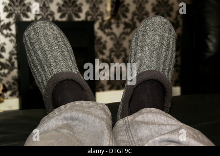 Uomo di piedi e gambe con pantofole sul poggiapiedi Foto Stock