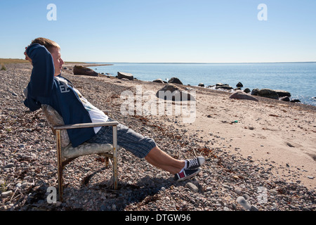 Giovane uomo adulto rilassarsi e sedersi sul banco vicino al mare e la visione a distanza. Foto Stock