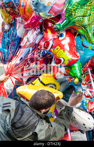 Un venditore di stallo cerca di controllare la sua grande collezione di elio palloncini pieni. Foto Stock