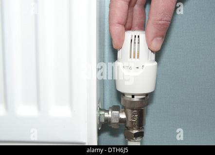 L'uomo ruotando il radiatore/valvola termostatica/controllo del riscaldamento su giù nel salotto di casa domestici, Inghilterra, Regno Unito (modello rilasciato) Foto Stock