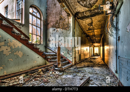 Corridoio in un edificio abbandonato, con la luce del sole che splende attraverso la finestra lontano Foto Stock