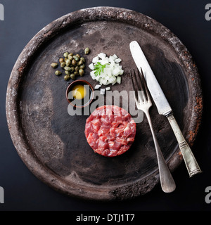 Tartare di manzo con capperi e cipolle fresche sul nero testurizzato sfondo Foto Stock