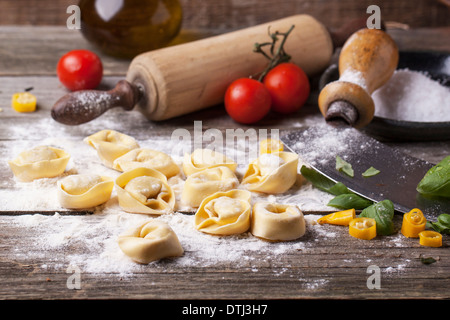 Pasta fatta in casa ravioli sul vecchio tavolo in legno con farina, basilico, pomodori e vintage accessori da cucina. Foto Stock
