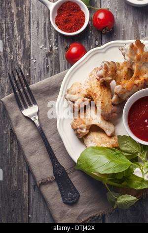 Vista dall'alto sulla piastra di grigliate di ali di pollo servito con profondo di pomodoro e basilico fresco su un vecchio tavolo di legno. Foto Stock