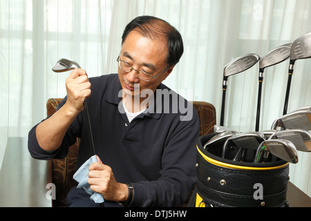 Uomo asiatico pulendo il suo golf club a casa Foto Stock