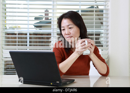Una donna asiatica che lavora da casa con una tazza di caffè Foto Stock