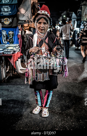 Lavoratore migrante. Anziana donna birmana etnica della tribù Akha collina che vende regali turistici in un mercato notturno tailandese. Thailandia S. E. Asia Foto Stock