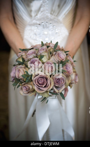 Una sposa in un abito bianco tenendo un mazzo di nozze di lavanda colorate di rose Foto Stock