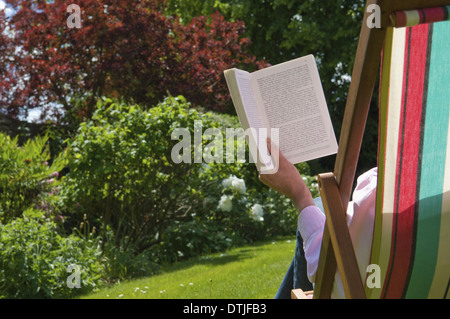 Una persona seduta in una sedia a sdraio lettura Gloucestershire in Inghilterra Foto Stock