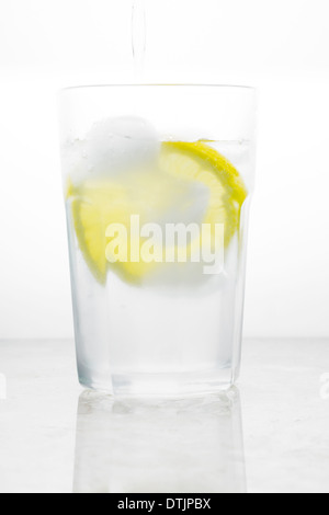 L'acqua versata nel bicchiere con ghiaccio e limone Foto Stock