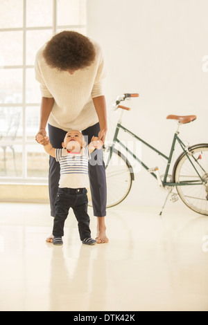 Madre aiutare baby boy a piedi in salotto Foto Stock