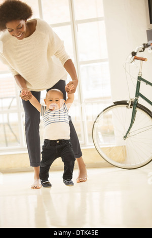 Madre aiutare baby boy a piedi in salotto Foto Stock