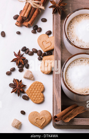 Due tazze di cappuccino servito con spezie e cookie come cuori sul panno bianco. Foto Stock