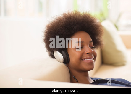 Donna in ascolto delle cuffie sul divano Foto Stock