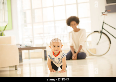 Madre guarda baby boy strisciare sul soggiorno piano Foto Stock