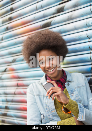 Donna con telefono cellulare sorridente contro il muro di graffiti Foto Stock