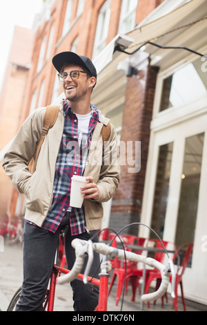 Uomo di bere il caffè in bicicletta sulla strada di città Foto Stock