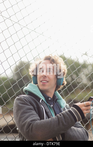 Uomo che ascolta le cuffie contro la catena collegamento recinto Foto Stock