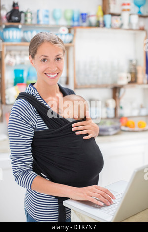 Madre con bambino utilizzando laptop in cucina Foto Stock