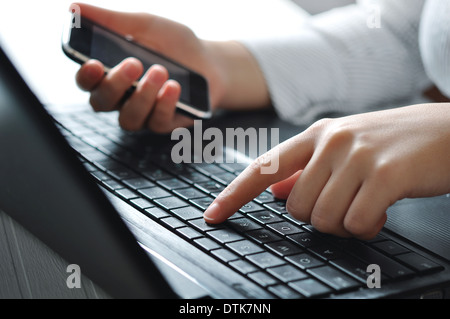Mani femminili utilizzando la tastiera portatile e azienda mobil phone Foto Stock