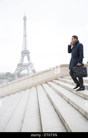 Imprenditore parlando al cellulare su passi vicino alla Torre Eiffel, Parigi, Francia Foto Stock