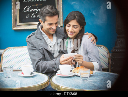 Giovane tramite telefono cellulare al cafè sul marciapiede, Parigi, Francia Foto Stock