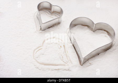 Due cookie cutter a forma di cuore sulla farina bianca Foto Stock