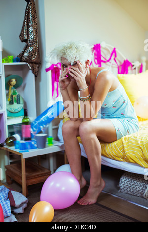 Hungover donna faccia di sfregamento sul letto la mattina dopo una festa Foto Stock
