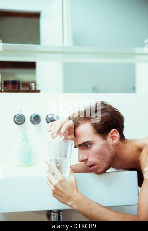 Hungover uomo guarda le compresse effervescenti in bagno Foto Stock