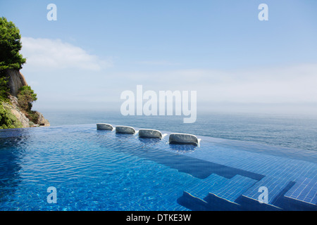 Sedie a sdraio in piscina a sfioro con vista sull'oceano Foto Stock