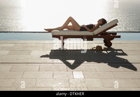 La donna a prendere il sole in sedia a sdraio a bordo piscina con vista sull'oceano Foto Stock
