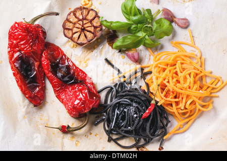 Vista dall'alto su nero e arancione spaghetti servita su sgualciti carta da forno con grigliate di paprica, aglio e basilico fresco. Vedere serie Foto Stock