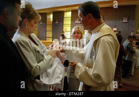 Vestita di un sacerdote cattolico saluta i genitori e i bambini durante le cerimonie di battesimo in una chiesa a Irvine, CA. Foto Stock