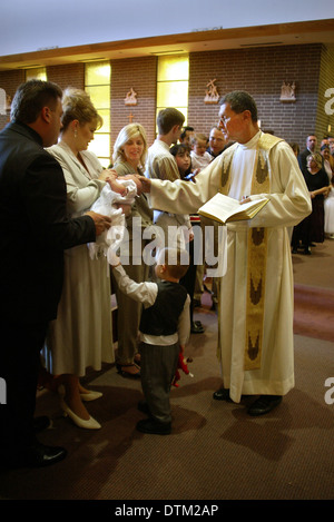 Vestita di un sacerdote cattolico saluta i genitori e i bambini durante le cerimonie di battesimo in una chiesa a Irvine, CA. Foto Stock