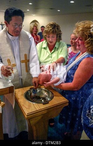 Un derubato cattoliche filippine sacerdote battezza una ragazza giovane con acqua santa presso il fonte battesimale della chiesa a Irvine, CA. Foto Stock