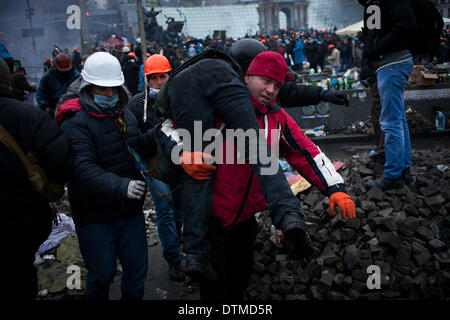 Kiev, Ucraina. Xx Febbraio 2014. I manifestanti portano un ferito i compagni di protester in Kiev. Centinaia di contestatori armati carica barricate della polizia giovedì di kiev central Piazza Indipendenza, nonostante una tregua chiamato poche ore prima dal paese del presidente merlata. Manifestanti hanno spinto la polizia indietro per circa 200 metri e sono state in controllo della maggior parte della piazza che avevano occupato all'inizio dell'Ucraina di tre-mese-vecchio crisi politica Credito: ZUMA Press, Inc./Alamy Live News Foto Stock