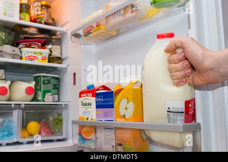 Una mano tirando fuori una bottiglia di plastica del latte da un fornitissimo porta frigo Foto Stock