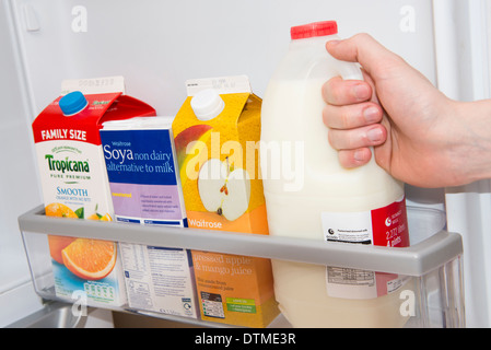 Una mano tirando fuori una bottiglia di latte da una porta frigo Foto Stock