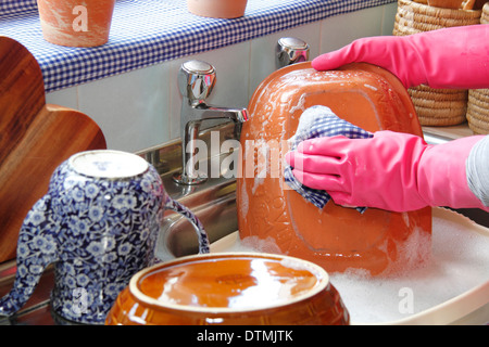 Donna che indossa guanti di gomma per lavare i bicchieri al lavello da cucina a casa Foto Stock