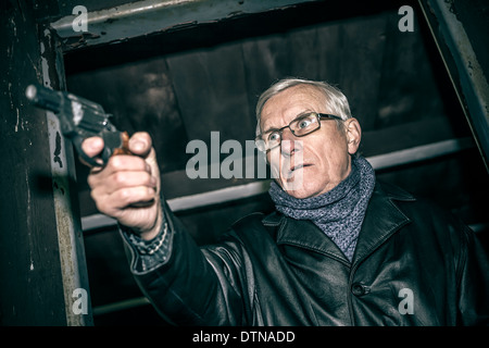 Pericoloso uomo senior puntando una pistola e in piedi nella vecchia cabina scuro. Foto Stock