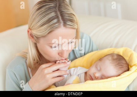 Madre sul divano baciare il suo bambino la mano Foto Stock