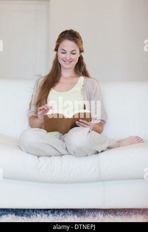 La donna gode di leggere un libro sul suo divano Foto Stock