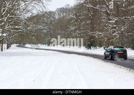 Unità auto lungo un vuoto di strada di campagna nei pressi di Bucklebury in presenza di neve, condizioni invernali. Berkshire, Inghilterra, GB, Regno Unito Foto Stock